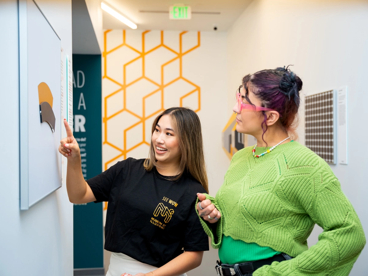 Two young women are looking at the Jastrow Illusion on the wall at Museum of Illusions Denver.